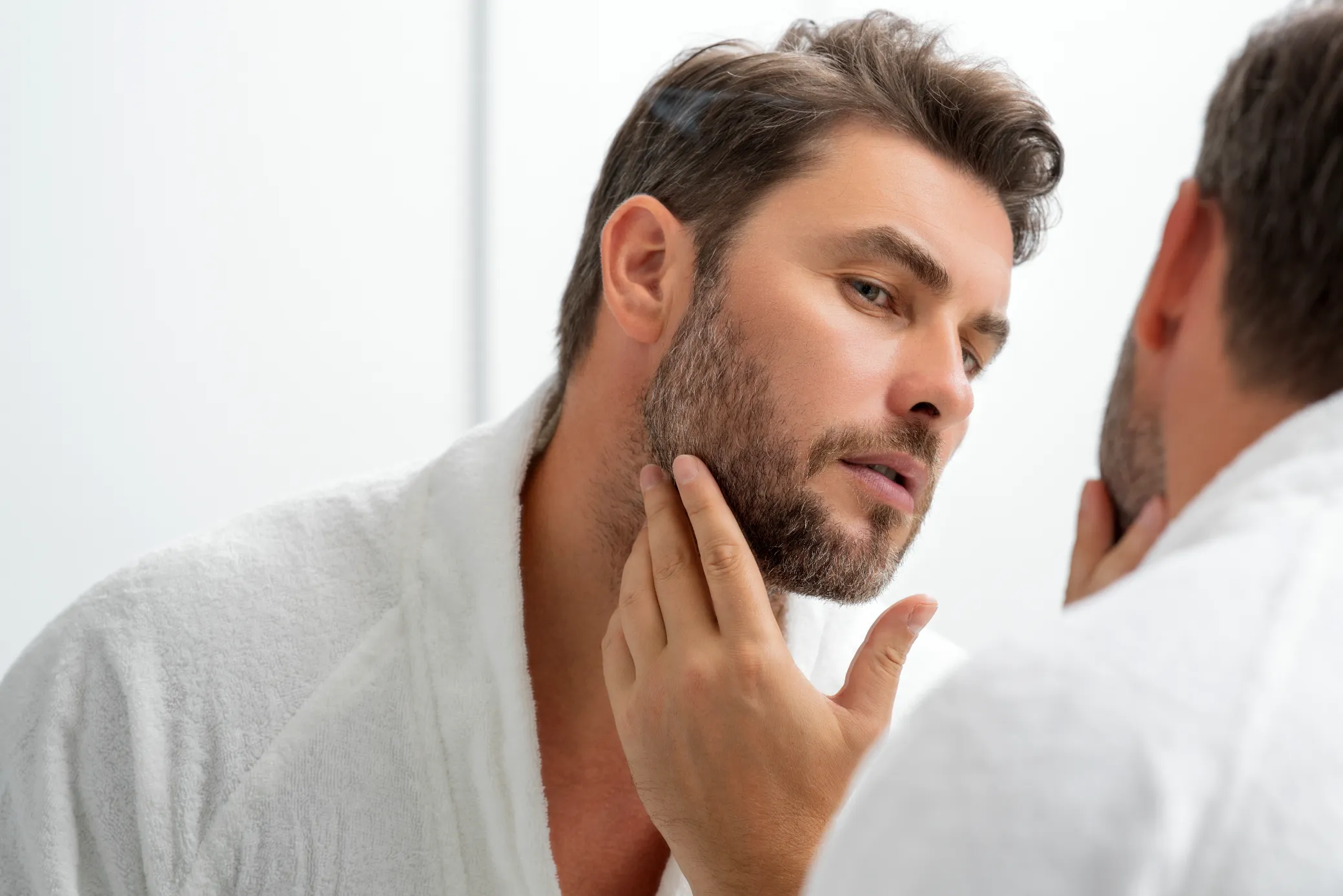 Man examining his facial appearance in a mirror reflecting the personalized care at a Colorado Springs medical aesthetics cl…
