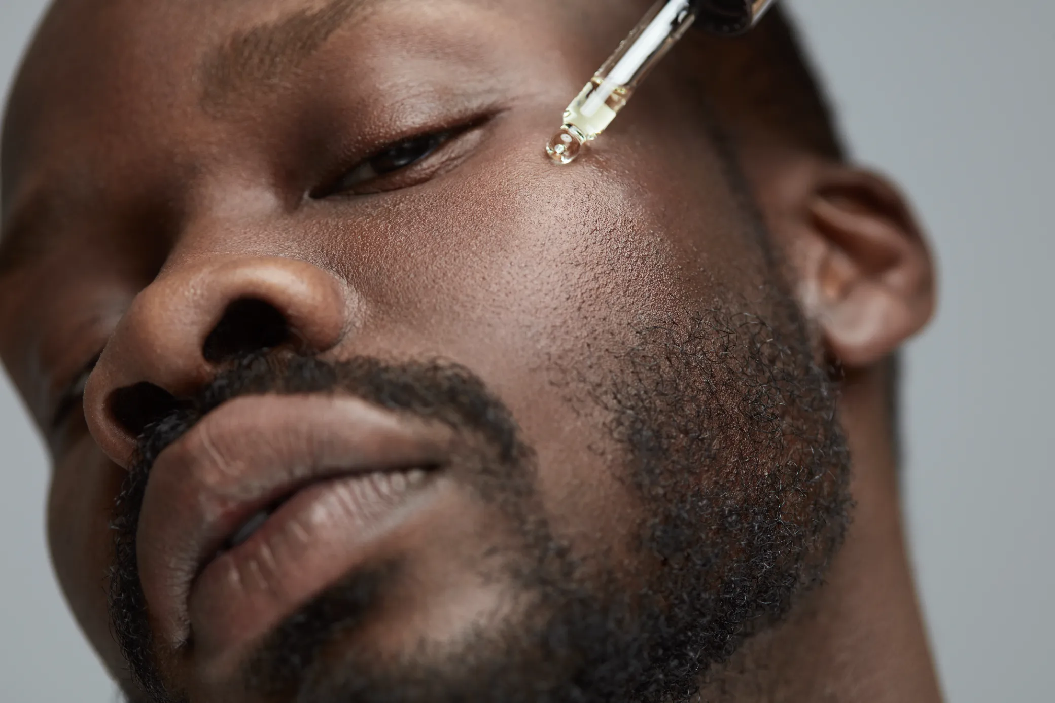 Man applying facial serum with dropper for skincare.