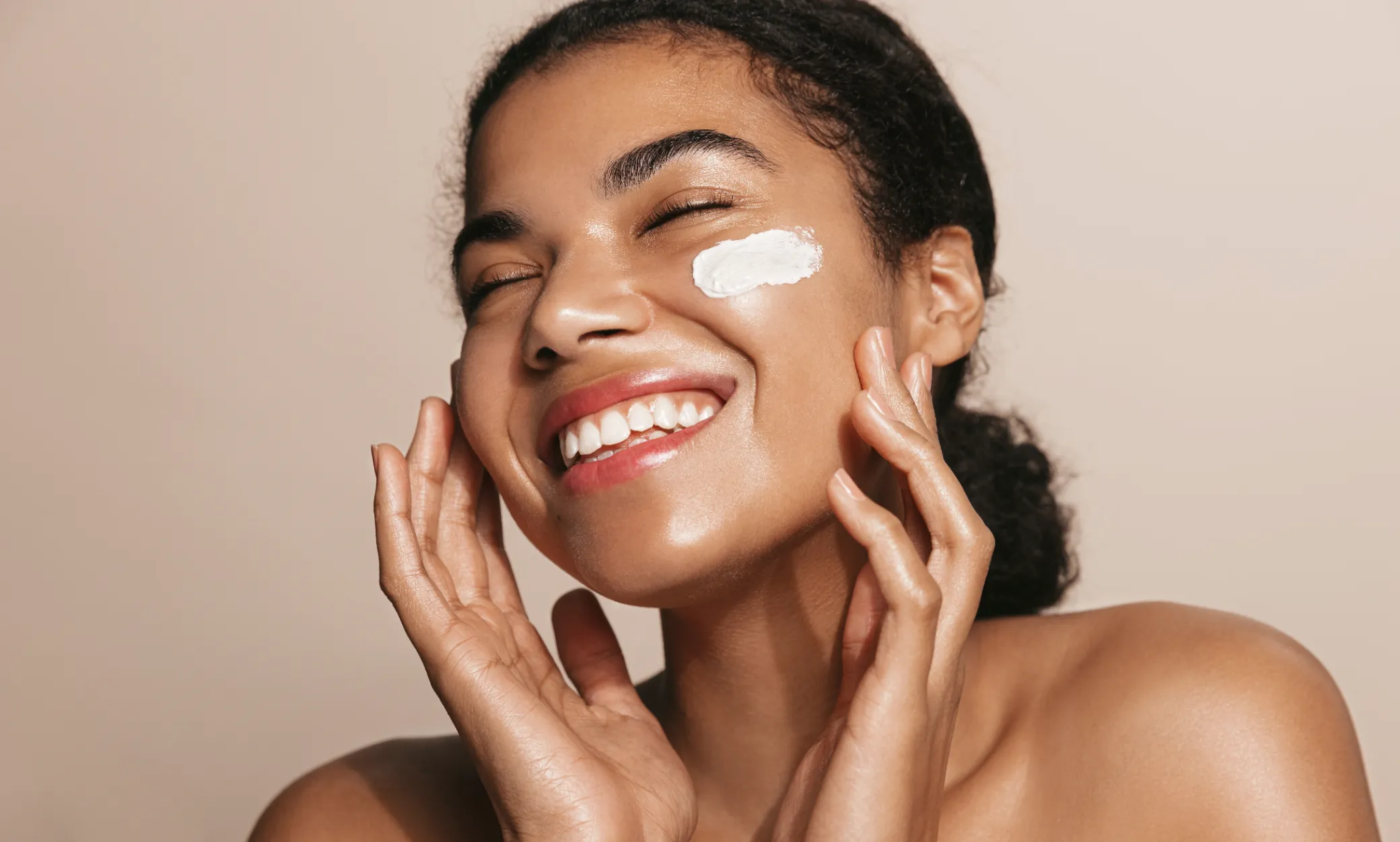 Woman joyfully applying skincare cream, reflecting personalized treatments at a Colorado Springs medical aesthetics clinic.