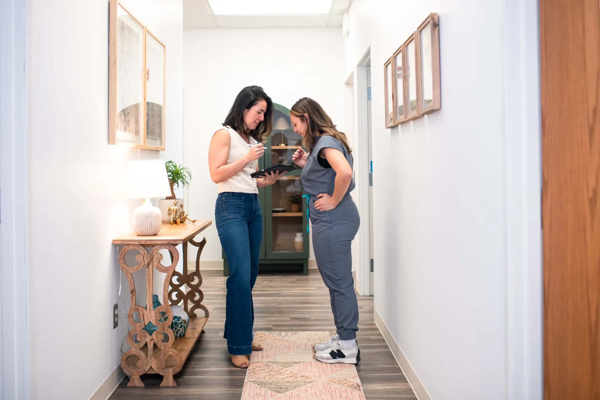 Two women discuss a tablet in a hallway at a Colorado Springs medical aesthetics clinic.