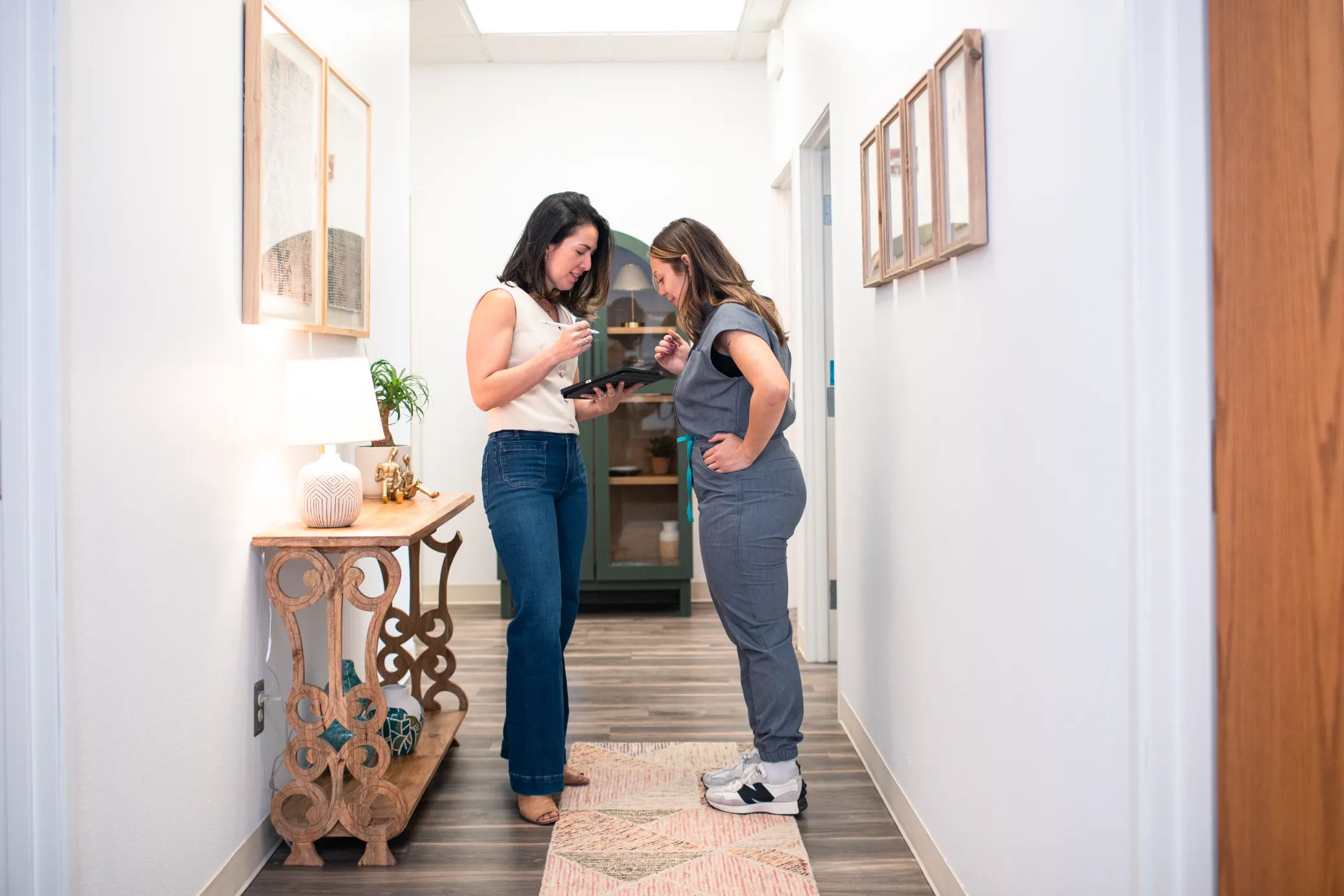 Two women discuss a tablet in a hallway at a Colorado Springs medical aesthetics clinic.