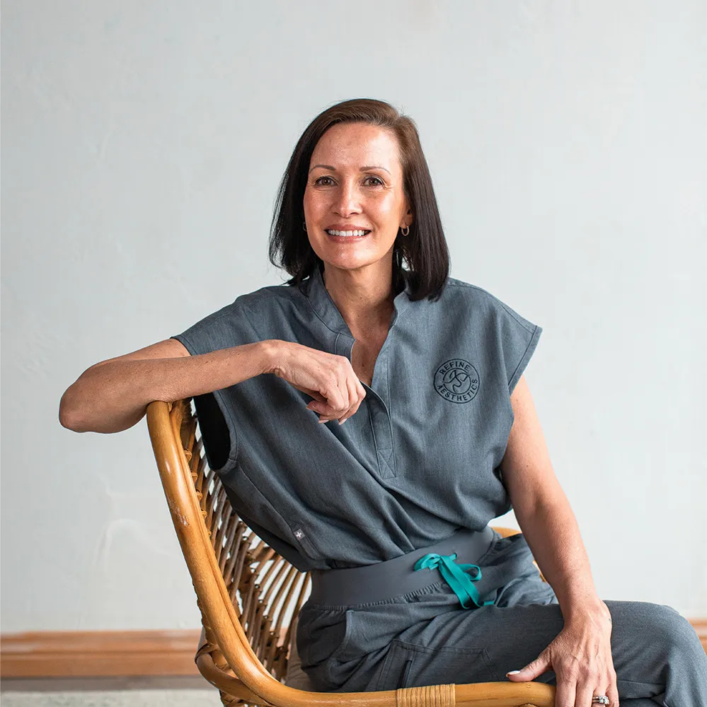 A staff member at Refine Aesthetics in Colorado Springs smiles while seated, representing personalized medical aesthetics ca…